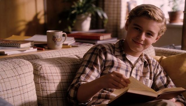 Teen reading on couch in plaid shirt turning page cozy sunlit home study moment with mug