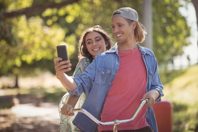 Happy couple looking at smart phone while riding bicycle against trees