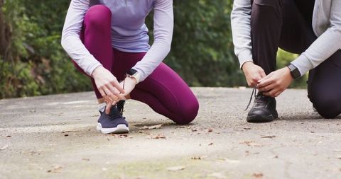 Couple tying running shoes on leafy woodland trail wearing smartwatches and athleticwear
