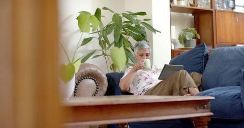 Senior Woman Relaxing on Couch with Tablet and Tea at Home