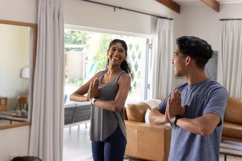 Sunlit african couple practicing partner yoga at home wearing activewear and smartwatches