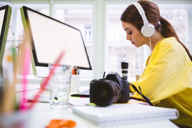 Side view of young female executive working with camera on desk at creative office