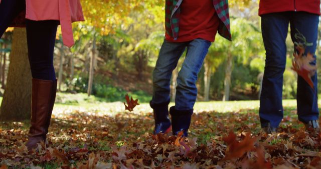 Two people are walking through a park covered with autumn leaves, with copy space. Their casual attire and the fallen leaves suggest a leisurely stroll during the fall season.