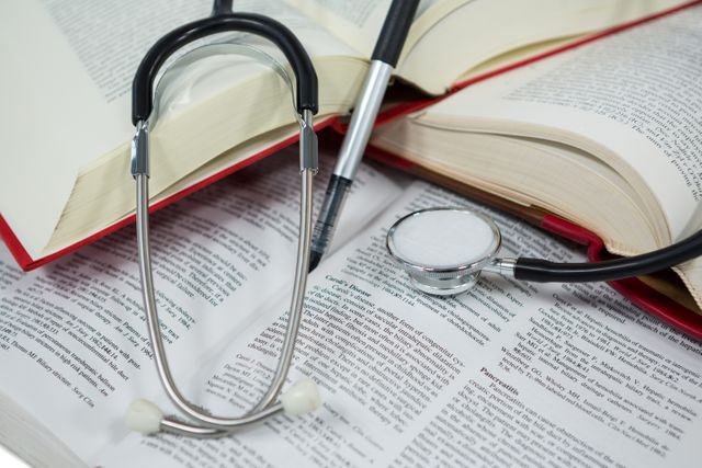 Stethoscope resting on open medical textbook with pen nearby. Ideal for illustrating medical education, healthcare studies, and research. Suitable for use in educational materials, medical training programs, and healthcare-related articles.
