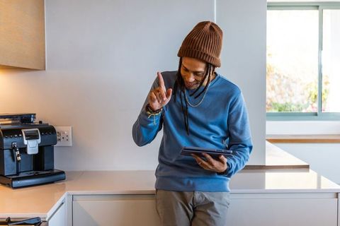 African american man leaning at kitchen counter tapping tablet near espresso machine