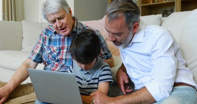 Grandfather, father, and young son using laptop at home. Grandfather and father assisting young boy in learning or discussing something on laptop, showcasing education, teamwork, and tech engagement with family. Ideal for themes of family, technology, and generational learning.