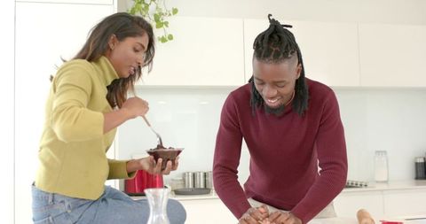 Multicultural couple baking in kitchen stirring chocolate and kneading dough together