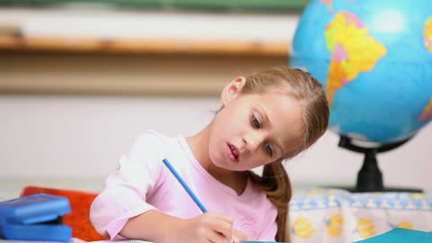 Young Student Writing in Classroom Next to Globe
