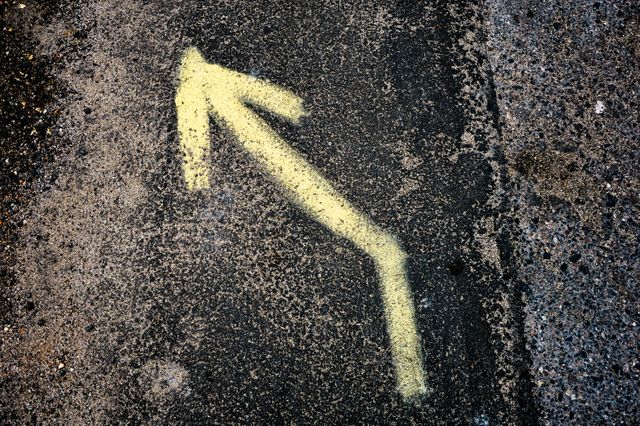 This scene features a yellow directional arrow painted on a rough asphalt surface. Ideal for projects related to travel, transportation, navigation systems, road safety initiatives, and urban infrastructure development. Provides a visual representation of guidance and direction in urban spaces.