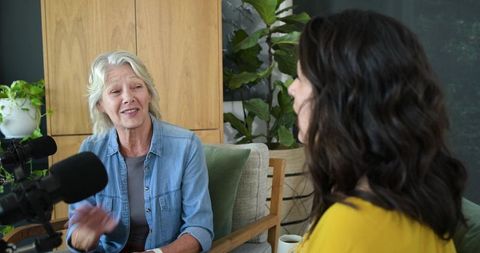 Senior woman sharing stories while recording podcast interview in cozy home studio lounge