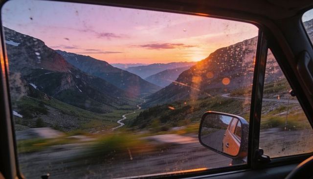 Sunset mountain valley with winding road through car window and rearview mirror at dusk