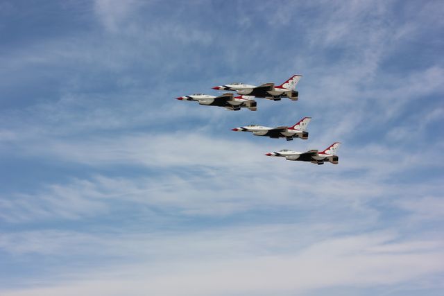 This image shows four jet planes flying in tight formation against a blue sky with wispy clouds. Ideal for use in articles about aviation, military airshows, precision flying techniques, and aeronautical engineering. It could also be used for promotional materials for airshows or military events, and by aviation enthusiasts in digital or print projects.