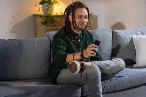 African american man relaxing on sofa holding remote control watching tv in cozy lounge