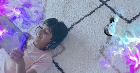 Smiling boy lying on plush rug using tablet with headphones and neon purple smoke effects