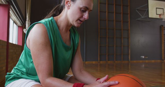 Caucasian female basketball player resting and holding ball. basketball, sports training at an indoor court.