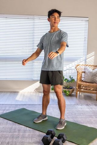 Asian man exercising on mat with hex dumbbells in sunlit living room for home fitness