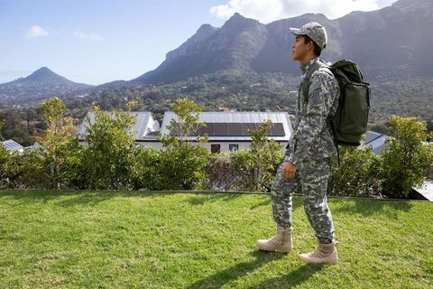Asian soldier walking on lawn with rucksack overlooking solar panels and mountain view