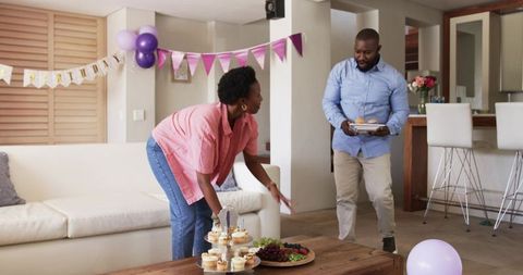 Couple preparing birthday celebration at home with cupcakes, balloons and floral decor