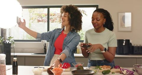 Diverse female friends filming and prepping vibrant salad at kitchen island with ring light