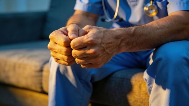 Healthcare worker clasping hands in blue scrubs showing fatigue, stress and quiet reflection