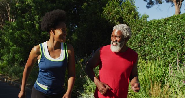 Smiling african american senior couple exercising outdoors running in sunny green road. healthy retirement and active lifestyle.
