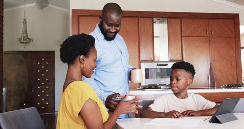 African American parents guiding child with tablet and smartphone during cozy kitchen morning