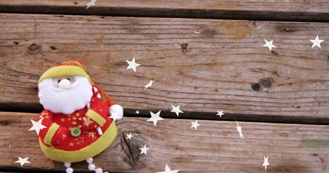 Plush santa doll resting on rustic wooden planks with floating white stars and copy space