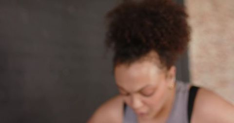 Curly bun woman leaning forward wearing grey sleeveless top and gold hoop earring