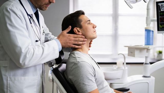 Doctor palpating patient neck during dental consultation in modern clinical office