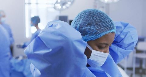 Female surgical staff adjusting hair net and tying gown in sterile operating room prep