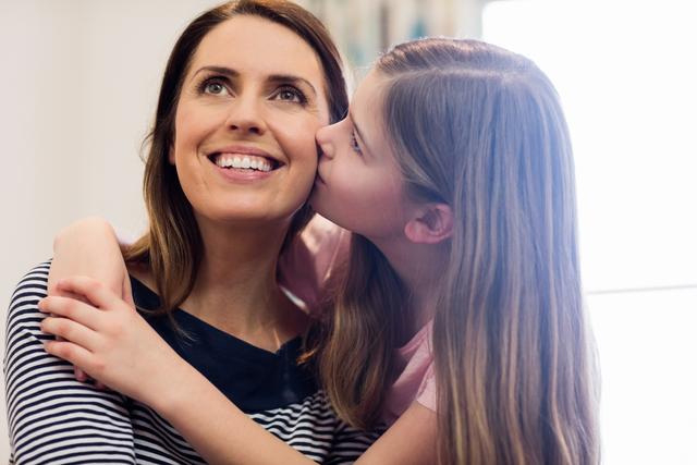 Affectionate daughter kissing her mother in living room at home
