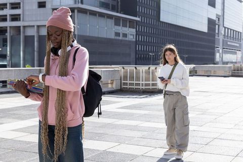 Urban students checking smartwatch and scrolling phone on city terrace with backpacks