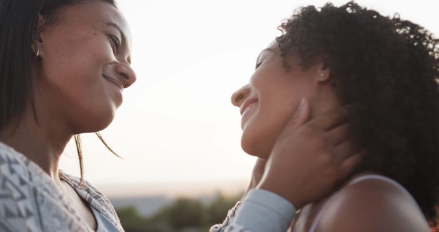 Romantic biracial lesbian couple smiling and embracing in garden at sundown, slow motion. Lifestyle, relationship, togetherness, love, relaxation and free time, unaltered.