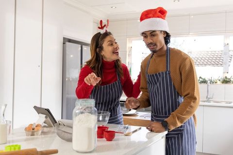 Festive mixed-ethnicity couple baking together in bright modern kitchen with tablet