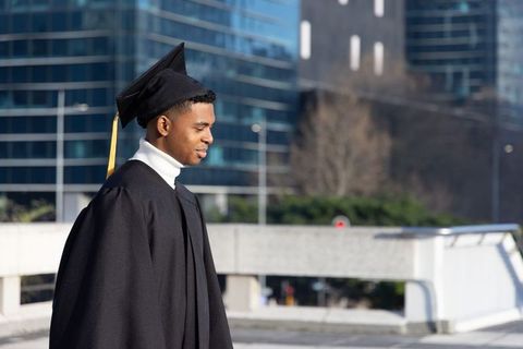 African american graduate on city rooftop wearing cap and gown celebrating milestone
