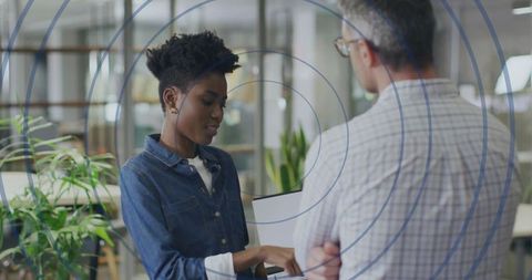 Woman presenting laptop chart to colleague in modern office with circular overlay