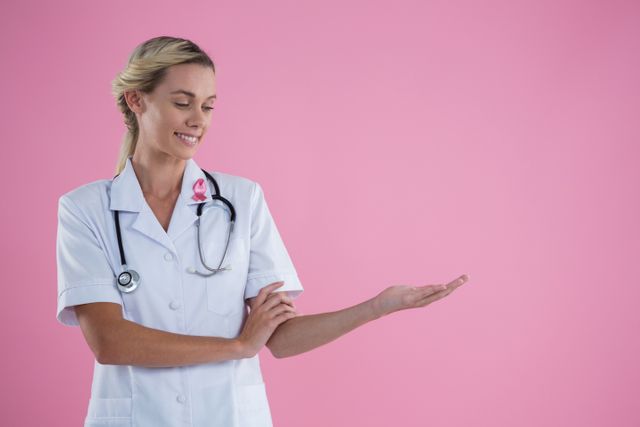 Smiling young female doctor gesturing while standing against pink background