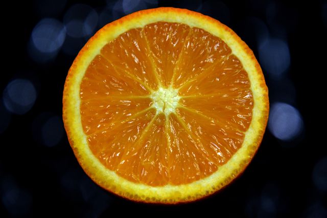 Close-up shot of a fresh orange slice against a black background showcasing its bright, juicy texture and vibrant colors. Ideal for health-related content, promoting healthy eating, vitamin C benefits, or visually appealing advertisements and food websites. Can also be used in citrus-themed designs, natural product promotions, or educational material on healthy eating habits.