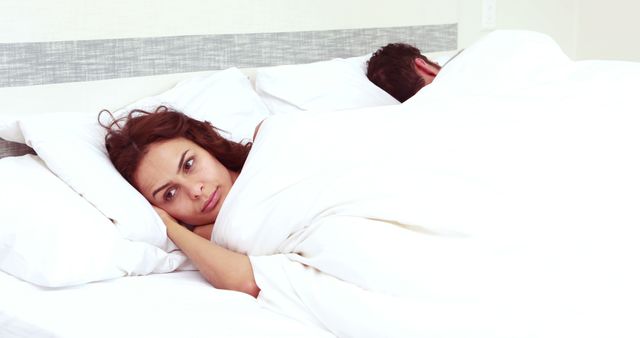 Troubled woman can't sleep while man is sleeping - Download Free Stock Photos Pikwizard.com