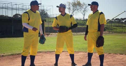 Sunlit baseball players talking on infield in yellow uniforms and navy caps