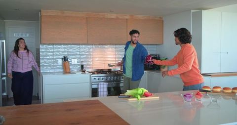 Diverse friends cooking together in modern kitchen sharing condiment bottle and laughing