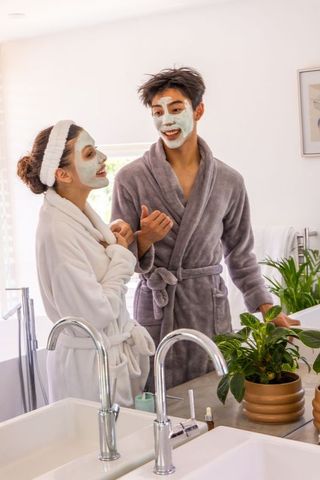 Diverse couple enjoying morning skincare ritual in bathrobes with clay face masks