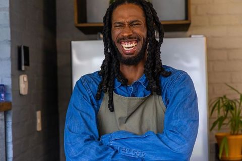 Laughing african american barista wearing apron and denim shirt in cozy café kitchen