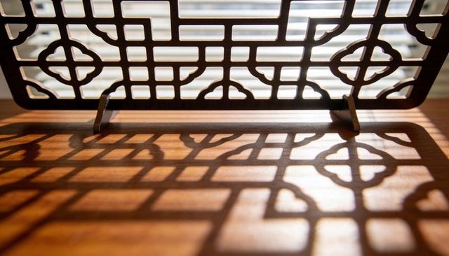 Sunlit wooden fretwork panel casting geometric lattice shadows across warm wood tabletop