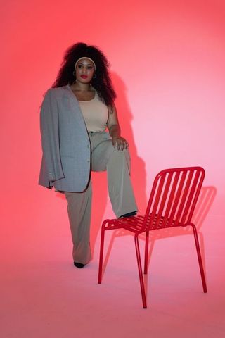 Confident african american woman posing draping blazer over shoulder with red chair