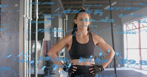 Female athlete standing hands on hips in gym with blue digital performance data overlays