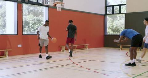 Diverse young men playing basketball in gym dribbling crossover driving to hoop