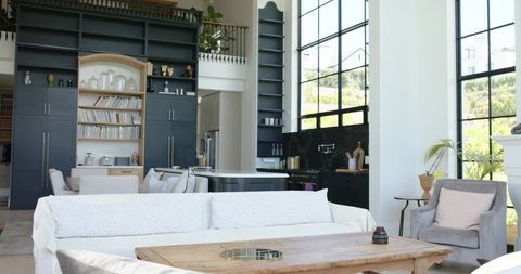 Bright double-height living room with white slipcovered sofa and black-framed windows