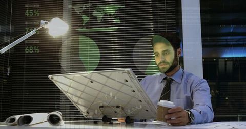 Business analyst working late holding coffee reviewing financial charts and city night view