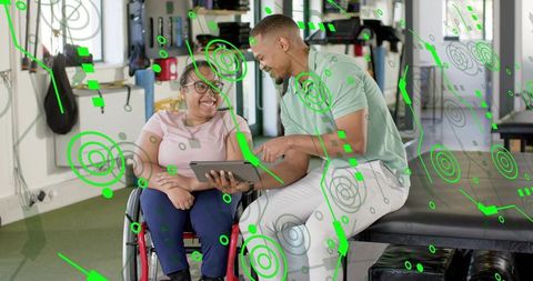 Smiling woman in wheelchair reviewing tablet with therapist in rehabilitation gym